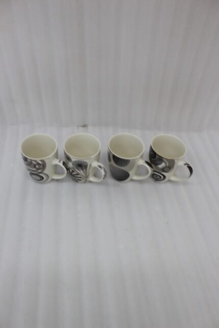 Set of 4 cream ceramic coffee mugs with distinct black geometric and swirl patterns displayed on a white marble countertop