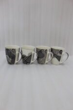 Set of 4 white ceramic coffee mugs featuring modern black geometric patterns lined up on a kitchen countertop.
