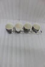 Set of 4 white ceramic coffee mugs featuring modern black geometric patterns lined up on a kitchen countertop.