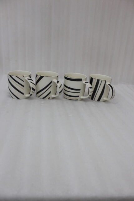 Set of 4 white ceramic coffee mugs featuring modern black stripes and subtle gold rim accents sitting on a granite kitchen countertop.