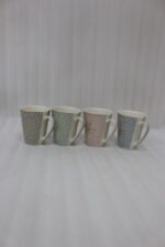 Four ceramic coffee mugs in beige, mint green, blush pink, and light blue with floral geometric patterns displayed on a marble countertop.