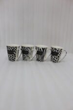 Set of four modern ceramic coffee mugs featuring black and white giraffe, zebra, and leopard prints with gold trim sitting on a marble kitchen counter.
