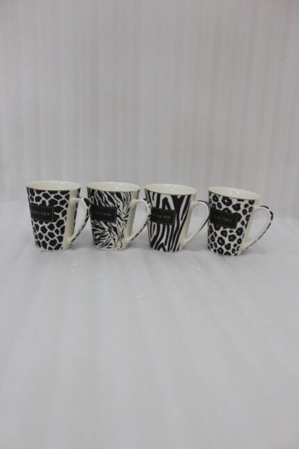 Set of four modern ceramic coffee mugs featuring black and white giraffe, zebra, and leopard prints with gold trim sitting on a marble kitchen counter.