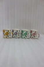 Four ceramic coffee mugs with colorful floral patterns in yellow, purple, green, and pink lined up on a marble countertop.