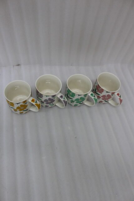 Four ceramic coffee mugs with colorful floral patterns in yellow, purple, green, and pink lined up on a marble countertop.