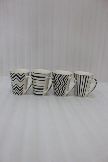 Set of four modern ceramic coffee mugs featuring black and white geometric, chevron, and striped patterns with gold rim accents on a marble countertop.