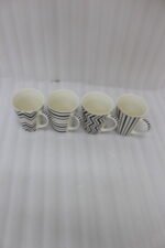Set of four modern ceramic coffee mugs featuring black and white geometric, chevron, and striped patterns with gold rim accents on a marble countertop.