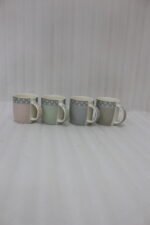 4-piece ceramic mug set in pink, green, and grey with polka dots, horizontal stripes, and gold rims on a kitchen countertop
