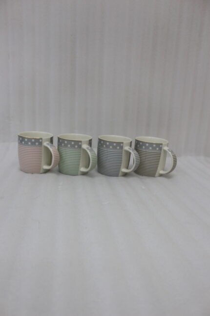 4-piece ceramic mug set in pink, green, and grey with polka dots, horizontal stripes, and gold rims on a kitchen countertop