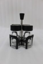 Four-piece clear glass spice jar set with lid options sitting in a black metal holder on a kitchen countertop.