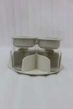 Four modern 6-piece revolving glass spice jar sets with gold trim lids displayed on a white kitchen countertop in beige, cream, black, and white colors.
