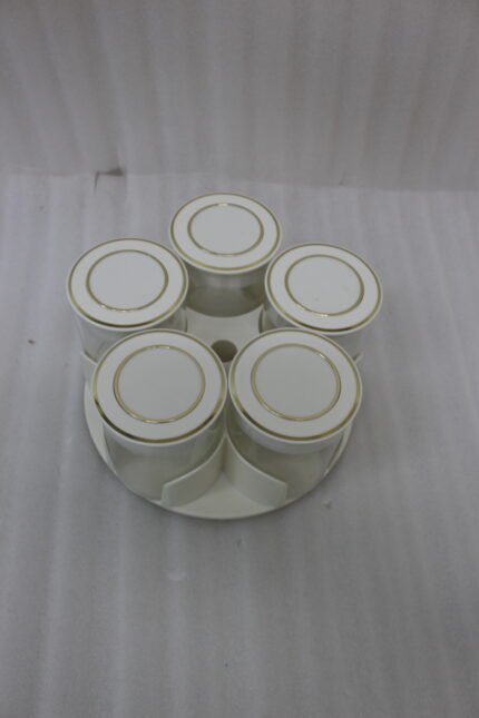 Four modern 6-piece revolving glass spice jar sets with gold trim lids displayed on a white kitchen countertop in beige, cream, black, and white colors.
