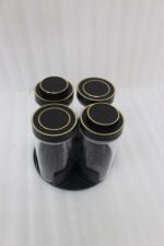 Four-piece clear glass spice jar sets with airtight lids displayed on rotating organizer trays in black, beige, tan, and white on a marble kitchen countertop.