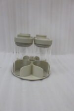 Four-piece clear glass spice jar sets with airtight lids displayed on rotating organizer trays in black, beige, tan, and white on a marble kitchen countertop.