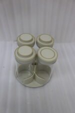 Four-piece clear glass spice jar sets with airtight lids displayed on rotating organizer trays in black, beige, tan, and white on a marble kitchen countertop.