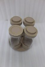 Four-piece clear glass spice jar sets with airtight lids displayed on rotating organizer trays in black, beige, tan, and white on a marble kitchen countertop.