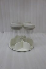 Four-piece clear glass spice jar sets with airtight lids displayed on rotating organizer trays in black, beige, tan, and white on a marble kitchen countertop.