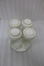 Four-piece clear glass spice jar sets with airtight lids displayed on rotating organizer trays in black, beige, tan, and white on a marble kitchen countertop.