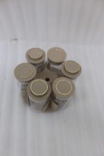 Modern rotating spice rack organizer set with 6 clear glass jars and gold-accented lids on a granite kitchen countertop.