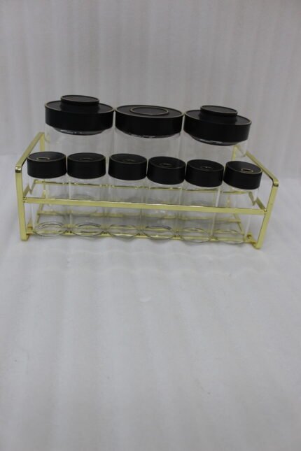 9-piece luxury glass spice jars with black gold-accented lids stored on a metallic gold wire rack on a marble kitchen countertop.