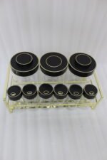 9-piece luxury glass spice jars with black gold-accented lids stored on a metallic gold wire rack on a marble kitchen countertop.