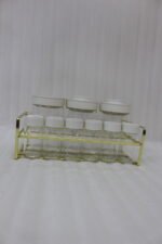 9-piece clear glass spice jar set with white and gold airtight lids arranged on a gold metal rack on a kitchen countertop.