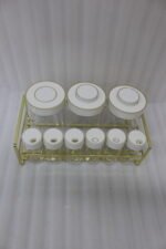 9-piece clear glass spice jar set with white and gold airtight lids arranged on a gold metal rack on a kitchen countertop.