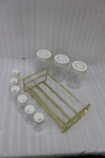 9-piece clear glass spice jar set with white and gold airtight lids arranged on a gold metal rack on a kitchen countertop.