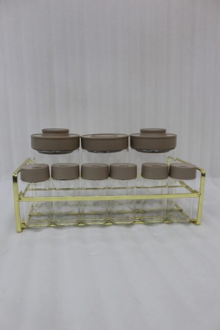 A 9-piece glass spice jar set with matte brown lids and gold-tone metal rack sitting on a granite countertop.