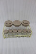 A 9-piece glass spice jar set with matte brown lids and gold-tone metal rack sitting on a granite countertop.