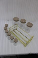 A 9-piece glass spice jar set with matte brown lids and gold-tone metal rack sitting on a granite countertop.