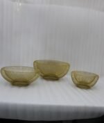 Set of three gold mesh decorative wire bowls sitting on a light wooden table in a brightly lit modern living room setup.