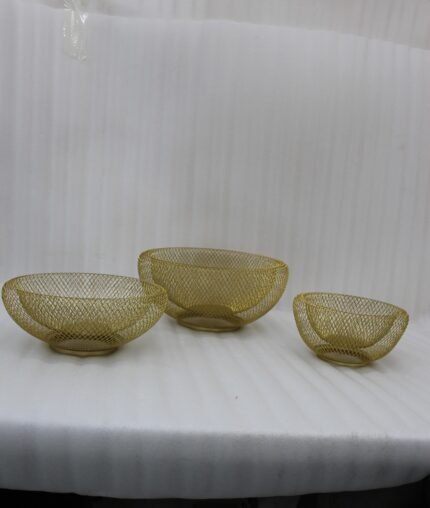 Set of three gold mesh decorative wire bowls sitting on a light wooden table in a brightly lit modern living room setup.