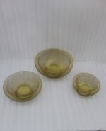 Set of three gold mesh decorative wire bowls sitting on a light wooden table in a brightly lit modern living room setup.