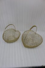 Two heart-shaped decorative gold wire mesh baskets with single handles set on a wooden table.