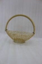 Gold decorative metal mesh basket with a curved wooden handle placed on a wooden table in a bright modern dining room