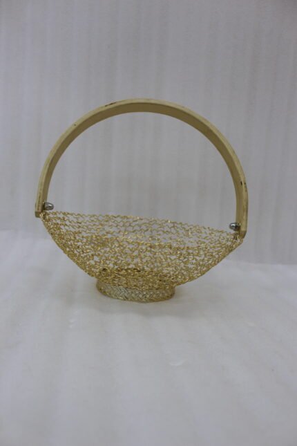Gold decorative metal mesh basket with a curved wooden handle placed on a wooden table in a bright modern dining room