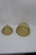 Two gold decorative metal wire mesh dome cloche covers sitting on a wooden table.