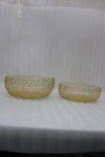 Set of two round gold woven wire decorative metal baskets sitting on a light wooden tabletop.