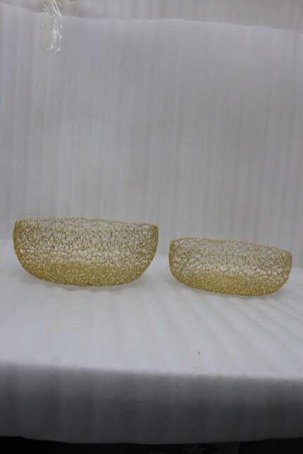 Set of two round gold woven wire decorative metal baskets sitting on a light wooden tabletop.