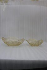 Two gold woven wire decorative metal baskets sitting on a light wooden tabletop.