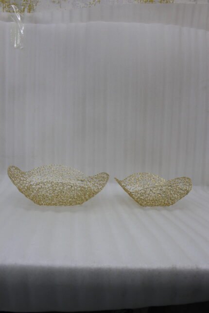 Two gold woven wire decorative metal baskets sitting on a light wooden tabletop.
