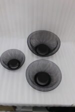 Set of three round black wire mesh decorative metal baskets displayed on a wooden kitchen countertop.