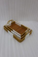 Set of three rectangular handwoven rattan serving trays with wooden bases and handles on a wooden table.
