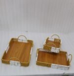 Set of three rectangular handwoven rattan serving trays with wooden bases and handles on a wooden table.