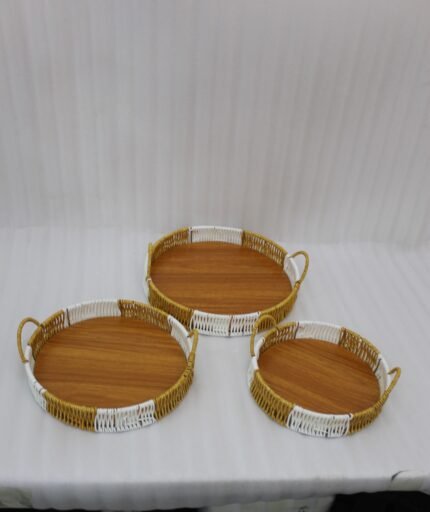 Three-piece round handwoven rattan serving tray set with white and tan woven edges and wooden bases on a light wood table.