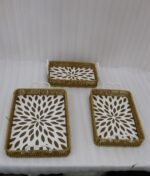 Three rectangular woven rattan serving trays with white decorative floral bottoms and side handles on a wooden table.
