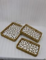 Three rectangular woven rattan serving trays with white decorative floral bottoms and side handles on a wooden table.