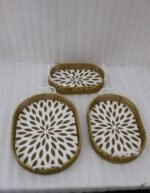 Set of 3 oval woven rattan serving trays with white handles and a modern geometric floral pattern base resting on a wooden table.