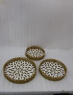 Set of 3 round handwoven rattan serving trays with white base patterns and handles resting on a wooden table